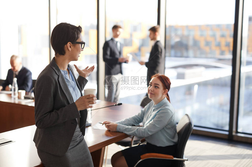 咖啡休息时在会议室聊天的两名年轻商业女青年的高角度肖像图片