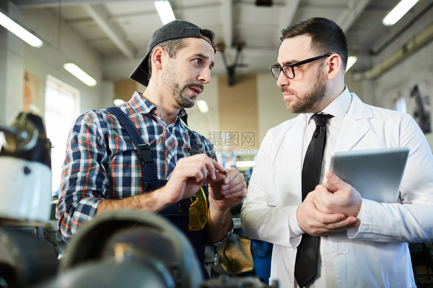 修理工在车间与站在机器单元旁的工厂人交谈的腰部肖图片