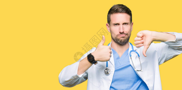 英俊的医生在孤立的背景下穿着医疗制服做拇指上下分歧和同意的表达图片