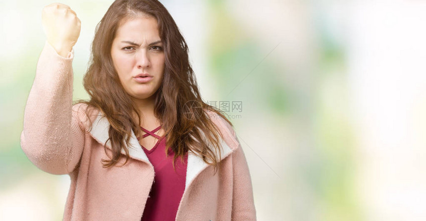 美丽的大码年轻女子穿着冬衣在孤立的背景下愤怒而疯狂地举起拳头沮丧和愤怒图片