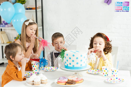 在庆祝生日时孩子们坐在桌边吃蛋糕和图片