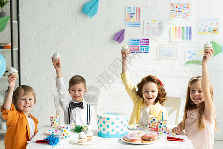 可爱的小孩坐在桌边一起庆祝生日时拿着纸杯蛋图片