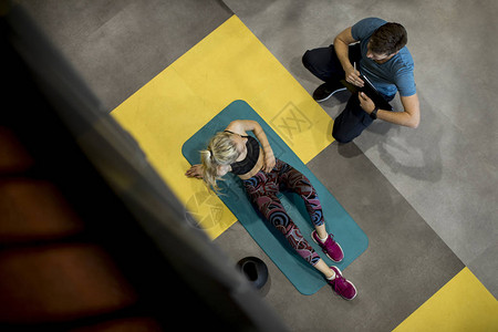 体育女运动员在健身房的个人教练帮助下进行锻图片