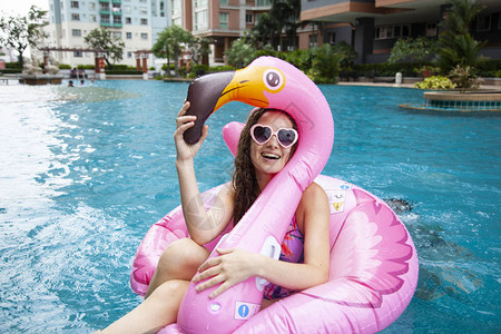 白种女人在游泳池里放松穿着粉红色火烈红的充气戒指图片