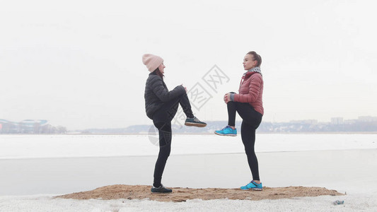 在雪滩上站着两个瘦弱的女人热身跑步把腿抬图片