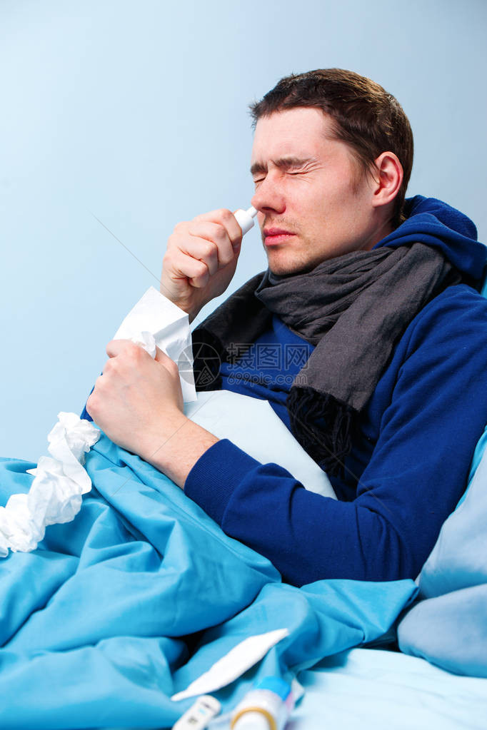 身着蓝枕头和毯子躺在床上时使用鼻喷剂的染色男病图片