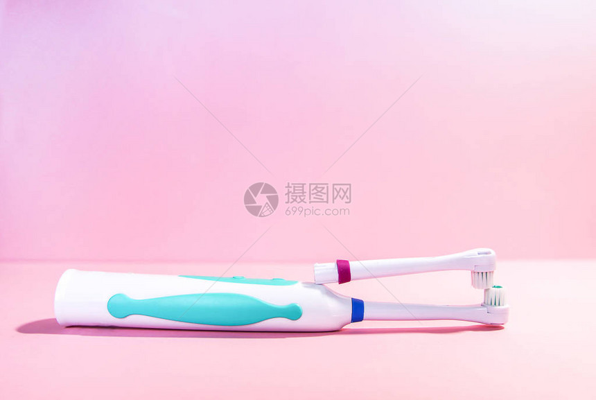 柔和的浅粉色背景上的两把电动牙刷图片