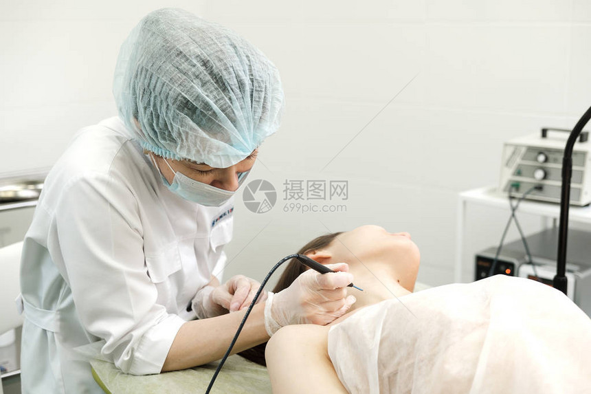 从女患者的脖子上去除胎记的医学治疗使用专业电烙器去除痣的女皮肤科医生无线电图片