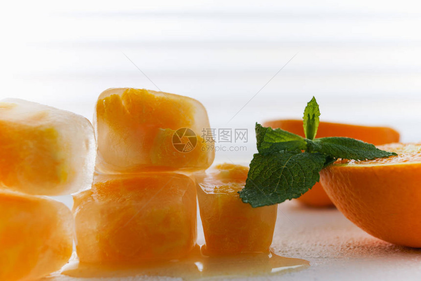 在冰块中冷冻的小片橙色水果和白色背景上的薄荷叶的特写图片