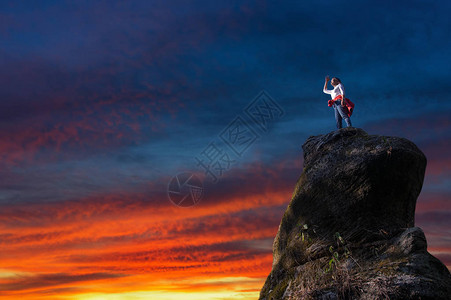 日落时站在岩石山峰上的女人图片