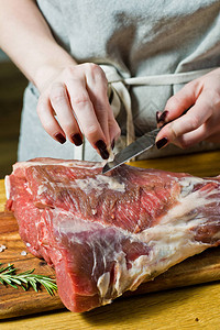 厨师在木制切削板上剪掉一块生山羊腿罗斯玛丽百香黑胡椒黑色背景顶层视图片