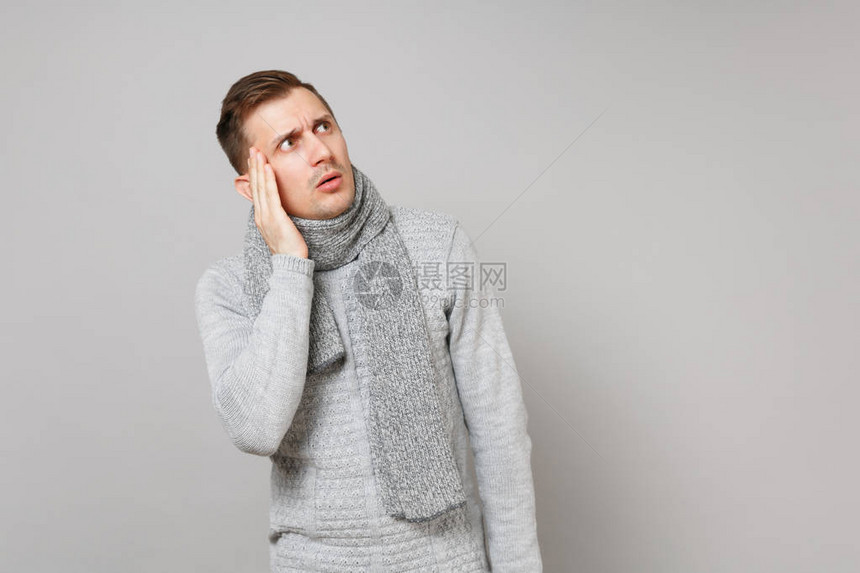 穿着灰色毛衣围巾贴近脸部在灰色背景上袖手旁观的年轻男子图片