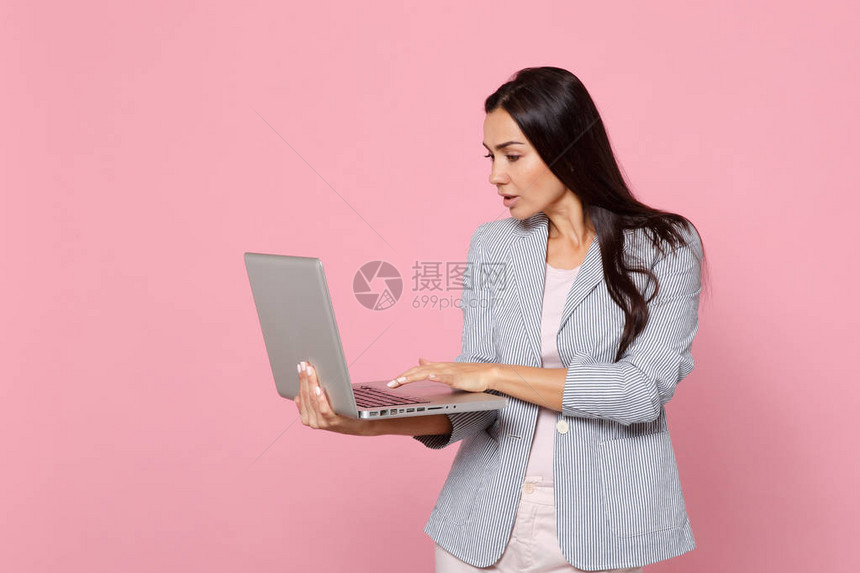 有吸引力的黑发年轻女子在条纹夹克使用笔记本电脑pc计算机隔离在工作室的粉红色柔和的墙壁背景上的肖像人们真诚的情感生活方式概念图片