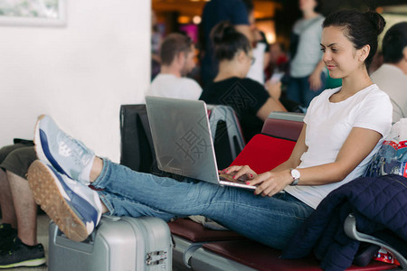 年轻女乘客在机场等待飞行时使用膝上型计算机图片
