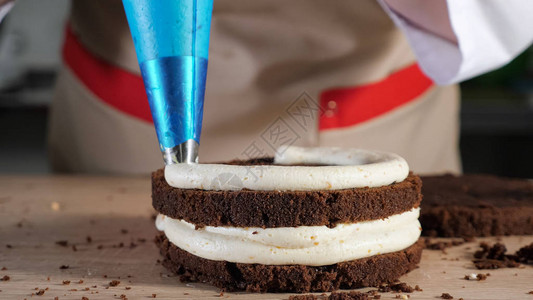 糕点厨师在巧克力海绵蛋糕上倒奶油加糕饼袋图片