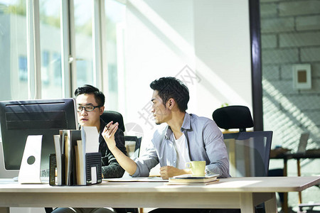 两个年轻的亚洲商人在办公室里一起讨论商业问题图片
