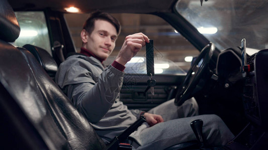 男驾驶员持钥匙坐在地下保险车厢的汽车上的照片图片