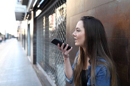 口授使用智能手机语音识别的青少年在街上用智能电话拍背景