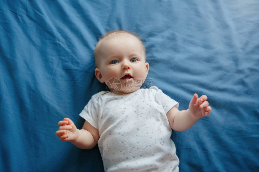 四个月大的蓝眼睛躺在床上看着相机的可爱微笑白人女婴的画像从上面看快乐的图片