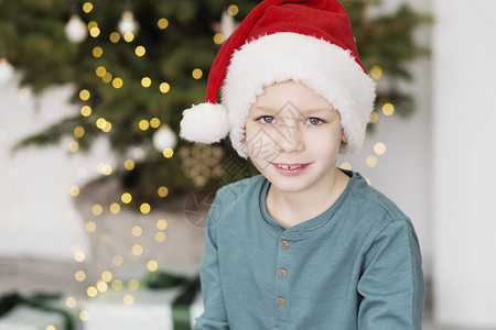 圣诞老人帽子的愉快的小男孩圣诞树前穿着圣诞服装的漂图片