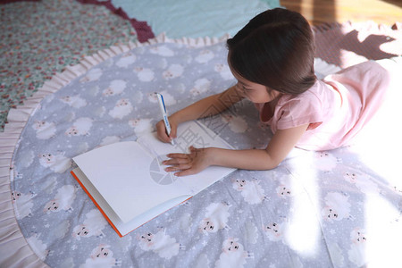 小女孩躺在圆垫上在画册上画图片