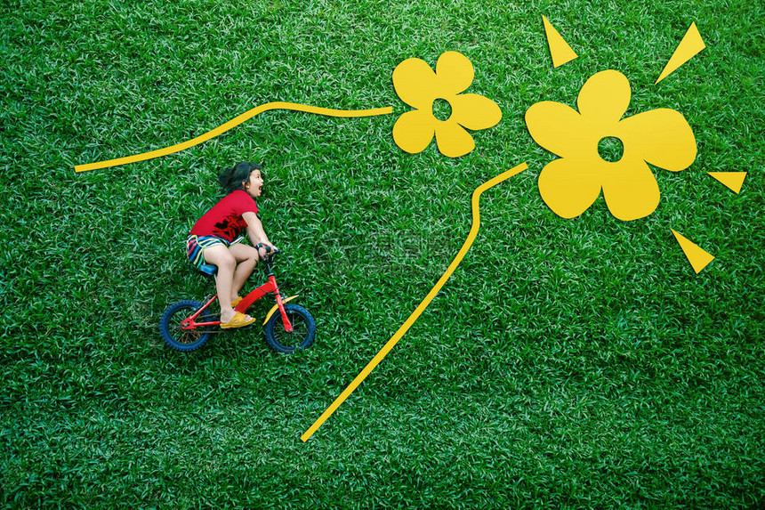 一个快乐的亚洲孩子的后视图骑自行车的女孩在春天或夏日的绿色草坪上躺下在她的户外活动中兴图片