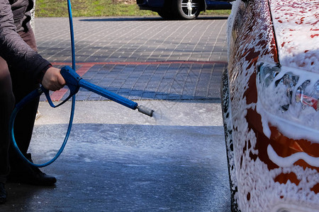 男人在洗车场洗他的橙色汽车在自助洗车场用肥皂清洗肥皂水流下来男图片
