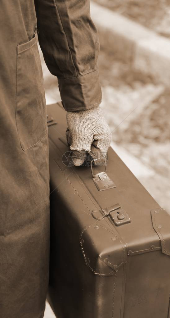 在出国旅行期间带旧皮手提箱和破手套的贫穷移民图片