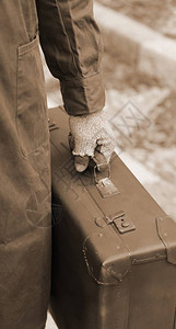 在出国旅行期间带旧皮手提箱和破手套的贫穷移民背景图片