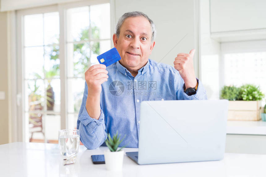 用信卡和笔记本电脑在家中指着点网上购物的英俊年长男子图片