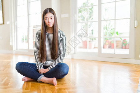 光着脚坐在家里地板上面部严重表情的美丽的亚洲妇女图片