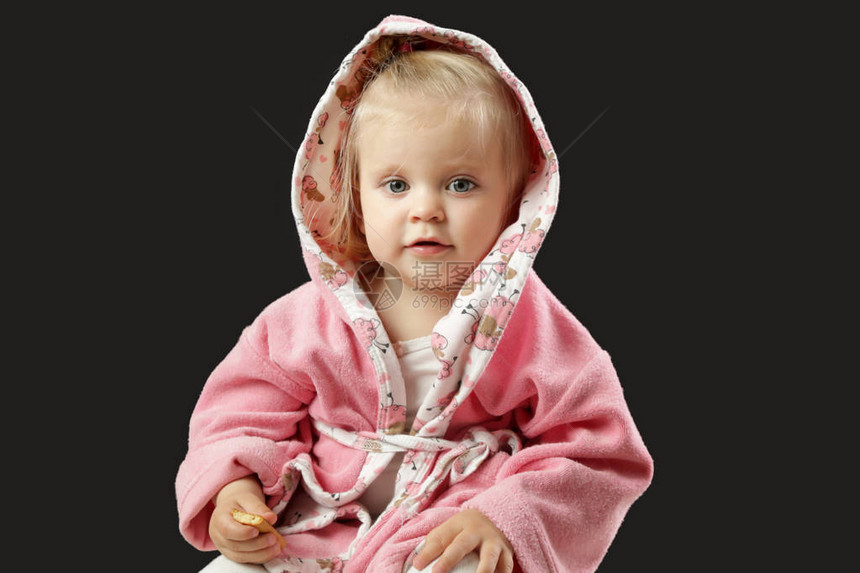 一个可爱的小女孩在洗完澡后坐在粉红色浴袍里拍着黑色图片