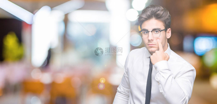 在孤立的背景下戴眼镜的年轻商人指着眼睛看着你的手势图片