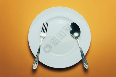 橙色背景上的白色碗和带勺子的叉子图片