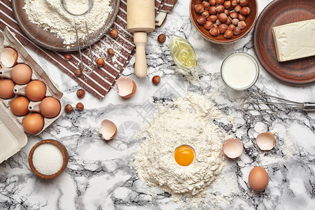 特写镜头大理石桌子背景上厨具和烘焙配料的顶部视图有一些鸡蛋和一个蛋壳图片