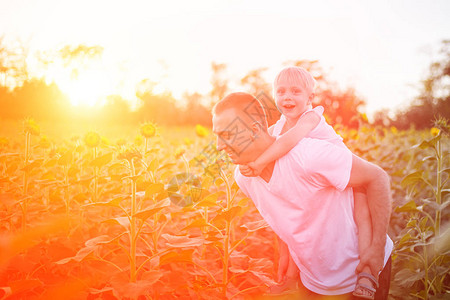 快乐的父亲和儿子背着在日落时在绿地上行走图片