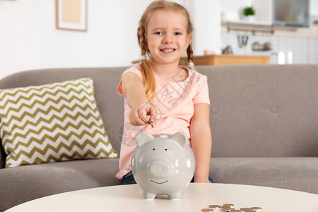 可爱的女孩把硬币放进小猪银行在图片