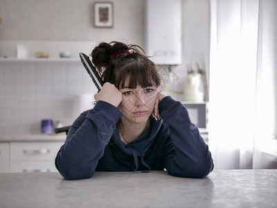 坐在厨房模糊背景的遥控器旁坐着无聊的年轻女士图片