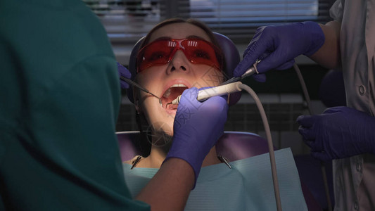 牙医正在使用电动牙刷照顾患者的牙齿病人附近有唾液喷射器的护士图片
