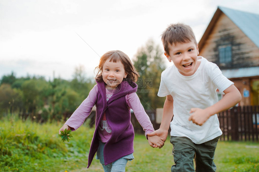 背景村屋里手牵的兄妹俩和祖母在村里度假孩子们男孩和女孩在户外玩得开心图片