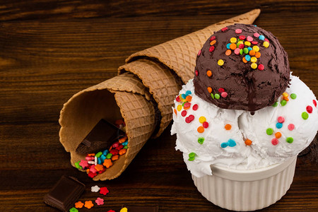 香草和巧克力冰淇淋勺还有喷洒和华夫饼蛋白在木制背景上图片