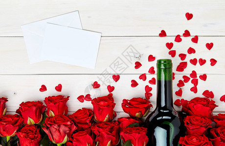 白色木质背景上的红玫瑰花蕾和一瓶酒图片