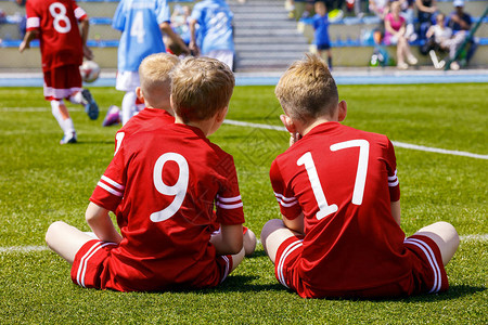一群孩子踢足球比赛两个身穿红色足球衣的年轻白人男孩坐在足球场的草图片