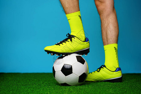 在绿草和蓝色背景上带球的足球运动员图片