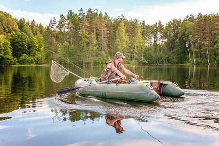 有钓鱼竿的渔夫在美丽的自然和湖泊或河流的背景下在橡皮艇上钓鱼露营旅游放松旅行积极生活背景图片