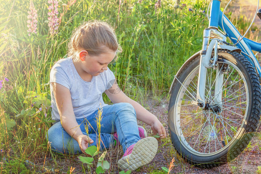 快乐的孩子坐在自行车附近在阳光明媚的夏日公园里骑自行车的年轻小女孩健康的学童夏季活动孩子们在户外玩图片