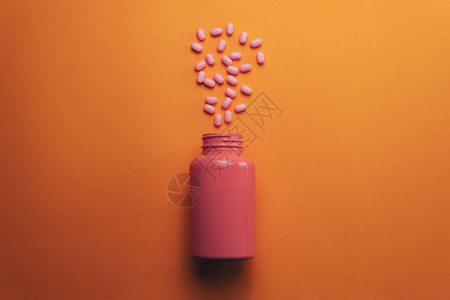 美丽的粉红色瓶子和粉红色药丸在橙色背景图片