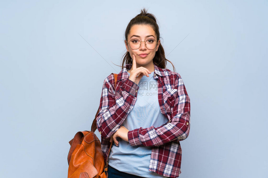 十几岁的学生女孩在孤立的蓝色墙壁前看图片