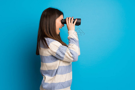 青春女子在蓝墙上与双目望远镜相图片