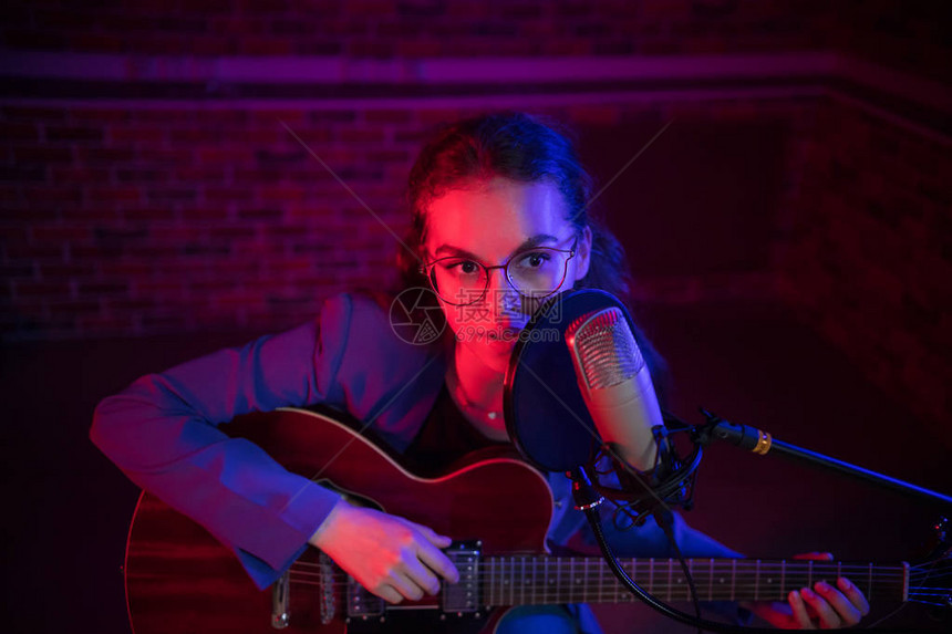 一个戴眼镜的年轻女子弹吉他唱着麦克风图片